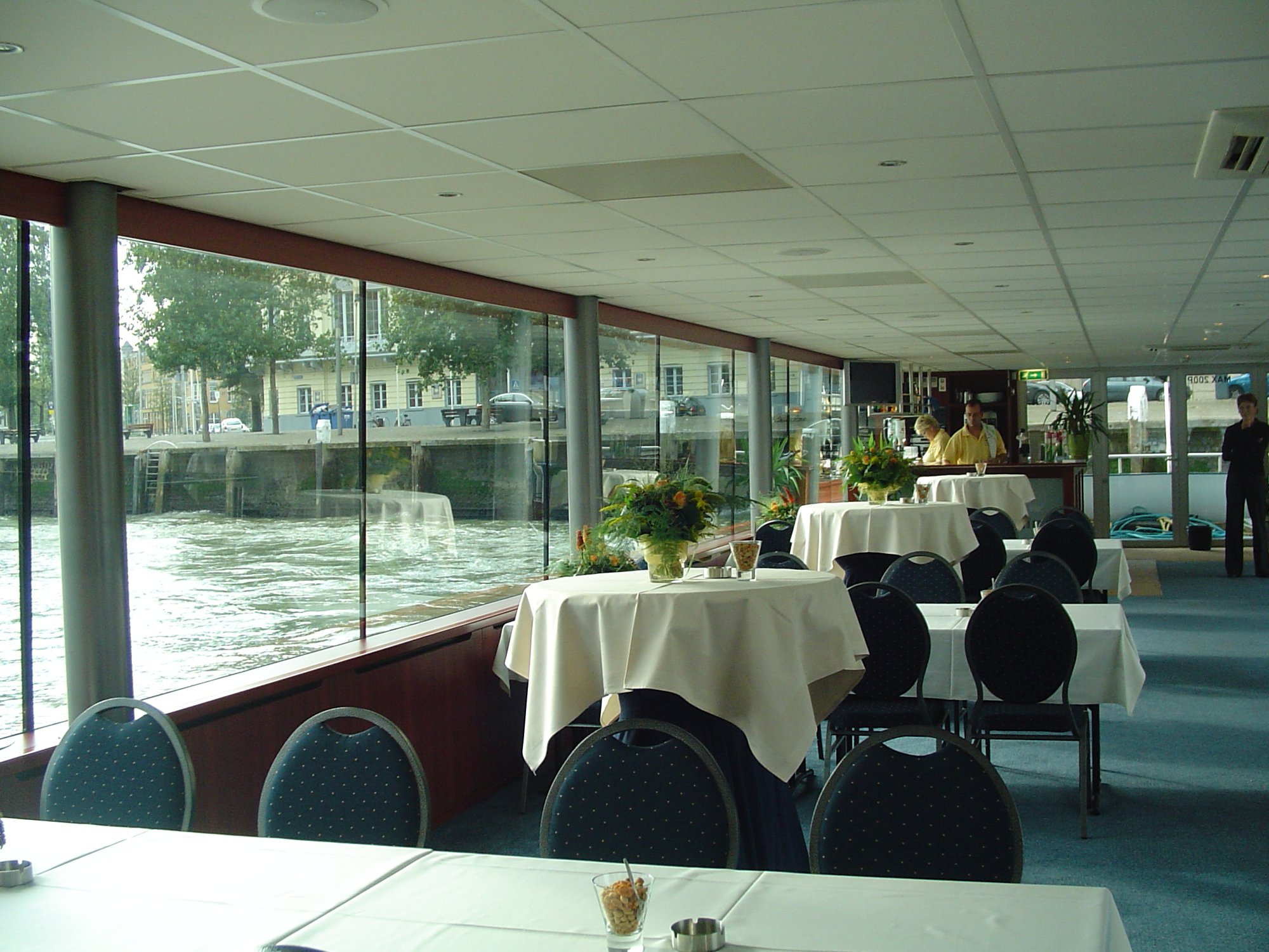 Restaurantzaal met witte gedekte tafels en waterzicht